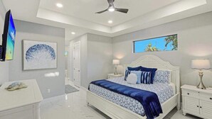 A bedroom with a bed, nightstands, a ceiling fan, artwork, and a view of the outdoors. - Canal front home with saltwater pool, hot tub, and washer and dryer. (Cape Coral)