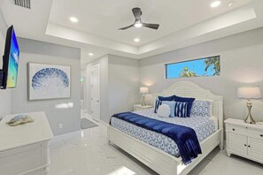 A bedroom with a bed, nightstands, a ceiling fan, artwork, and a view of the outdoors. - Canal front home with saltwater pool, hot tub, and washer and dryer. (Cape Coral)