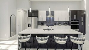 A modern kitchen with a central island, bar stools, and a backsplash with a geometric pattern. - Canal front home with saltwater pool, hot tub, and washer and dryer. (Cape Coral)