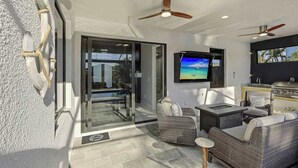 An outdoor patio with wicker furniture, a TV, ceiling fans, and a grill. - Canal front home with saltwater pool, hot tub, and washer and dryer. (Cape Coral)