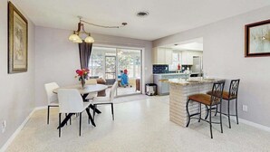 A modern kitchen with a central island, a dining area with a round table and chairs, and a view of the outside through large windows. - Dog-friendly home w/access to Englewood Beach, WIFI, and outdoor patio (Englewood)
