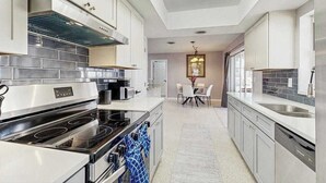 A modern kitchen with stainless steel appliances, white cabinetry, and a dining area with a chandelier. - Dog-friendly home w/access to Englewood Beach, WIFI, and outdoor patio (Englewood)