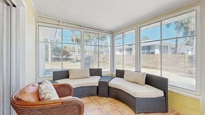 A sunroom with a curved sofa and chair, large windows, and a tiled floor. - Dog-friendly home w/access to Englewood Beach, WIFI, and outdoor patio (Englewood)