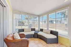 Un solárium con sofá curvo y sillón, ventanas amplias y suelo de baldosas.
