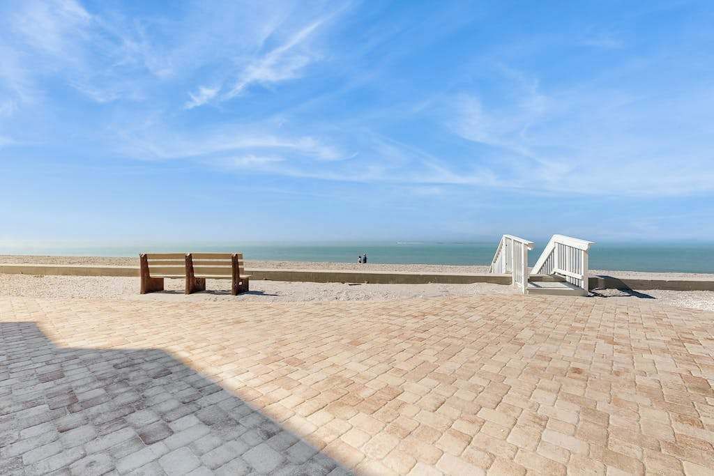 A paved beach area with a wooden bench and a white railing.