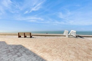 Una zona de playa pavimentada con un banco de madera y una barandilla blanca.
