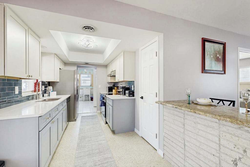 A modern kitchen with white cabinetry, a central island, and a dining area with a table and chairs.
