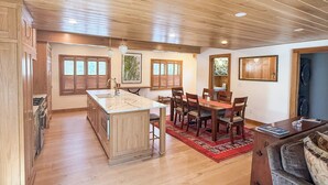 A spacious kitchen with wooden cabinetry, a central island, and a dining area with a red rug. - Camp Ridgewood- Spacious 6-bedroom house in lovely Bolton Landing with AC (Bolton Landing)