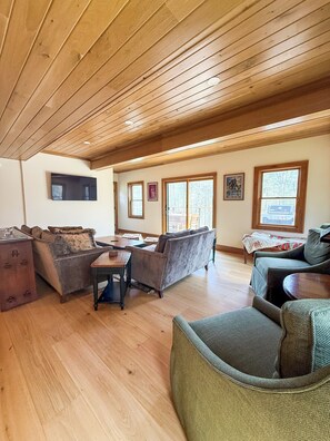 Ein geräumiges Wohnzimmer mit Holzböden, Holzzieldecke und großen Fenstern.