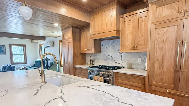 A kitchen with wooden cabinets, a marble countertop, a gas stove, and pendant lighting. - Camp Ridgewood- Spacious 6-bedroom house in lovely Bolton Landing with AC (Bolton Landing)