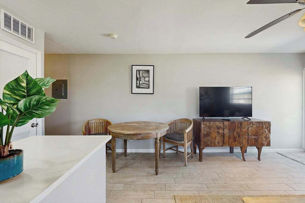 Een eethoek met een ronde houten tafel, twee stoelen, een televisie op een houten kast en een potplant.
