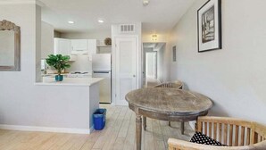 Una cucina moderna con mobili bianchi, un'area pranzo con un tavolo rotondo e sedie in legno, e un corridoio che conduce a un'altra stanza.