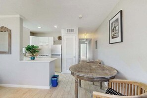 A modern kitchen with white cabinets, a dining area with a round table and wooden chairs, and a hallway leading to another room. - Spacious master duplex w full kitchen, close to beach & shopping (Naples)