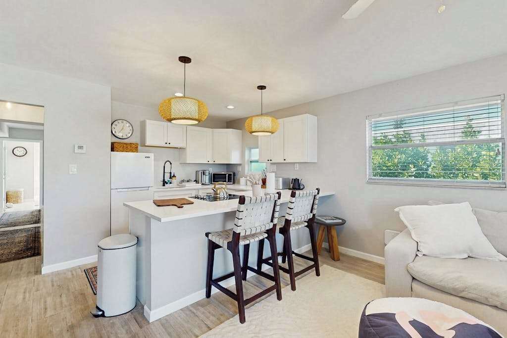 A modern kitchen with white cabinets, a central island, bar stools, and pendant lighting.