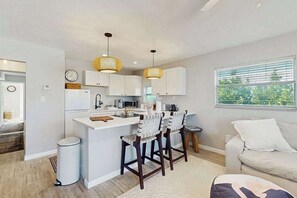 A modern kitchen with white cabinets, a central island, bar stools, and pendant lighting.