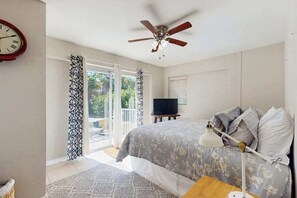A bedroom with a bed, a ceiling fan, a TV, and a window with curtains.