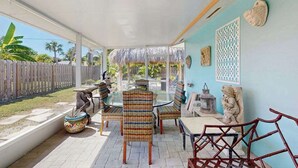Eine überdachte Terrasse mit einem Glastisch und gestreiften Stühlen, einem Holzzaun und einer Statue an der Wand.