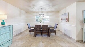 A dining area with a table and chairs, a hanging light fixture, a window, and a painting on the wall. - Coastal retreat steps to the beach with screened lanai and bikes (Englewood)