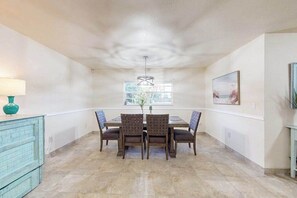 A dining area with a table and chairs, a hanging light fixture, a window, and a painting on the wall. - Coastal retreat steps to the beach with screened lanai and bikes (Englewood)