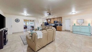 A spacious living area with a sofa, a television, and a kitchen in the background. - Coastal retreat steps to the beach with screened lanai and bikes (Englewood)