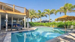 Ein Swimmingpool mit Liegestühlen, einer überdachten Terrasse und Palmen.