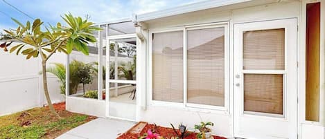 A house with a covered porch, a small garden with plants and a tree, and a sliding glass door.