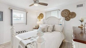 Quarto com cama, ventoinha no teto, janela e detalhes decorativos nas paredes.