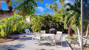 An outdoor patio with a round table and chairs, surrounded by lush greenery and palm trees. - Dog-friendly duplex with outdoor living area - walk to beach/downtown (Venice)
