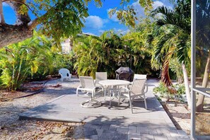 An outdoor patio with a round table and chairs, surrounded by lush greenery and palm trees. - Dog-friendly duplex with outdoor living area - walk to beach/downtown (Venice)