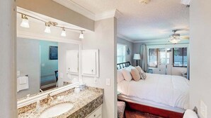 A bedroom with a bed, a nightstand, a window, and a bathroom with a sink and mirror. - Home with private pool, enclosed yard, patio, sunroom, AC, & W/D (Venice)