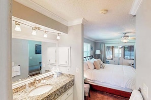 A bedroom with a bed, a nightstand, a window, and a bathroom with a sink and mirror. - Home with private pool, enclosed yard, patio, sunroom, AC, & W/D (Venice)