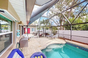 A covered outdoor swimming pool with lounge chairs and a patio area. - Home with private pool, enclosed yard, patio, sunroom, AC, & W/D (Venice)