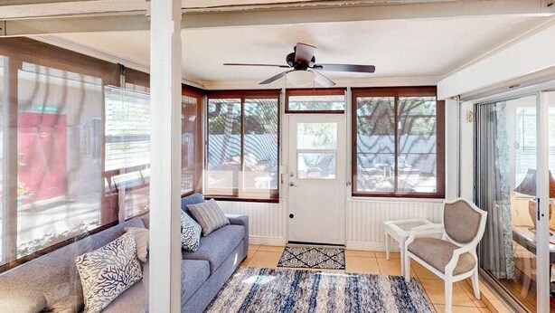 A room with a sofa, a chair, a ceiling fan, and large windows. - Home with private pool, enclosed yard, patio, sunroom, AC, & W/D (Venice)