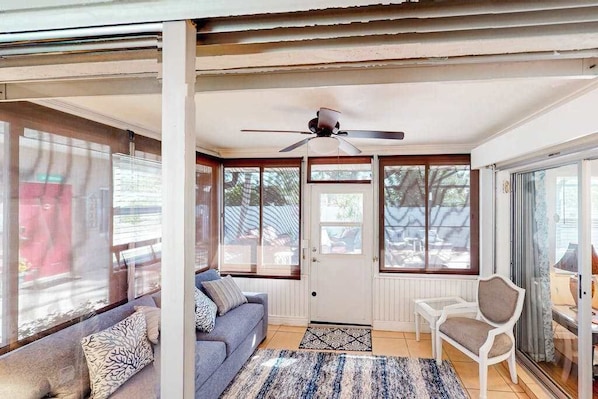 A room with a sofa, a chair, a ceiling fan, and large windows. - Home with private pool, enclosed yard, patio, sunroom, AC, & W/D (Venice)