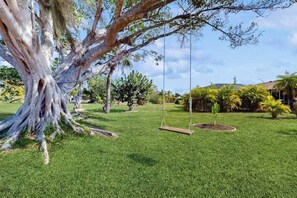 A well-maintained lawn with a large tree, a swing set, and various shrubs and plants. - Coastal home with private, saltwater pool, gas grill, and internet (Punta Gorda)