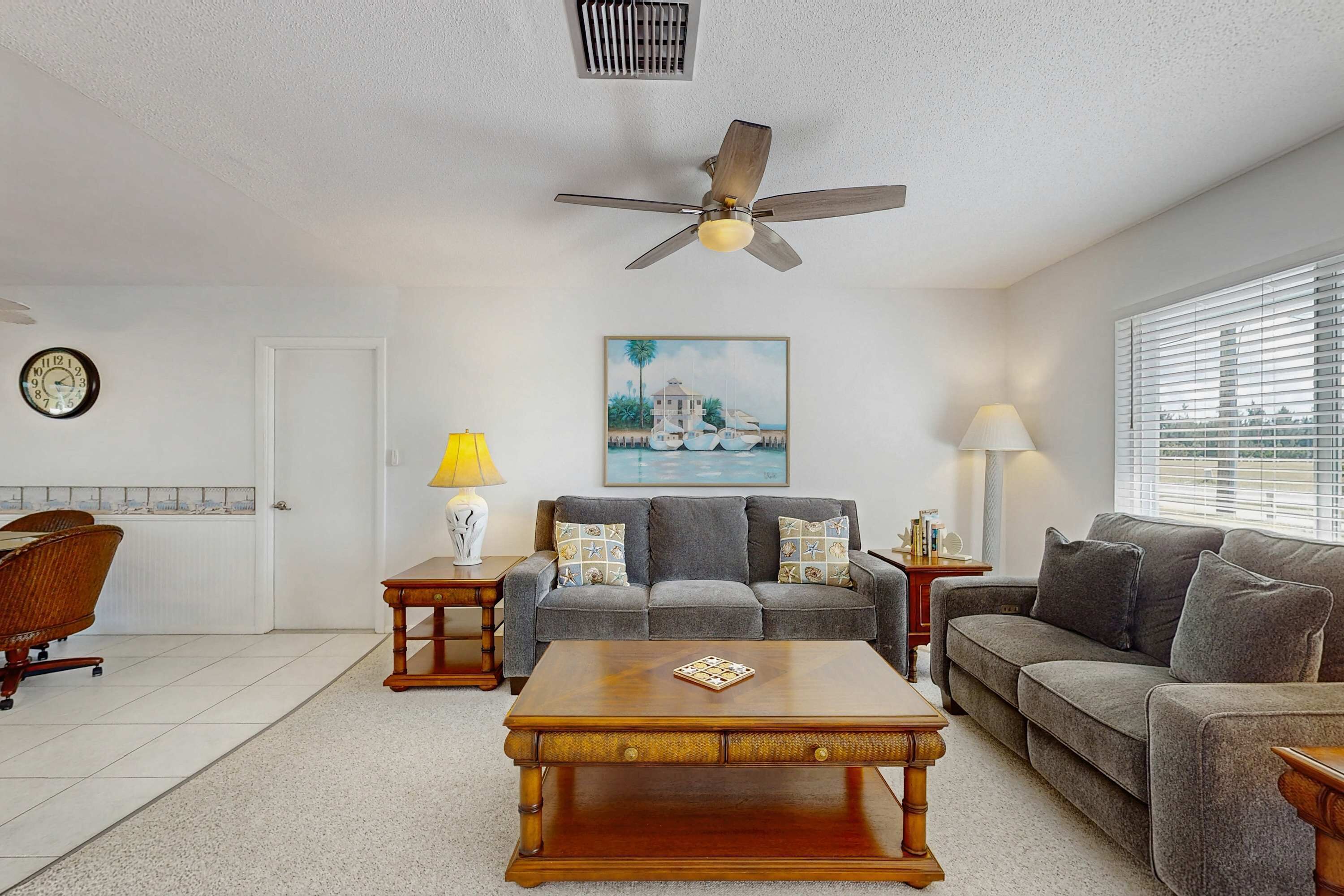 A living room with a sofa, coffee table, two lamps, a clock, and a ceiling fan.