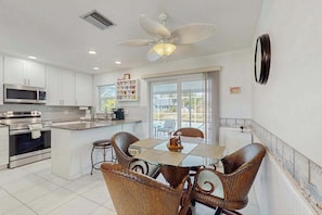 A kitchen with white cabinets, a microwave, an oven, a dining table with wicker chairs, and a ceiling fan. - Coastal home with private, saltwater pool, gas grill, and internet (Punta Gorda)