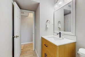 A modern bathroom with a white sink, wooden vanity, and a large mirror. - Coastal duplex with full kitchen, close to beach & shopping (Naples)