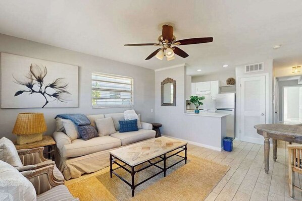 A living room with a sofa, coffee table, and artwork on the wall. - Coastal duplex with full kitchen, close to beach & shopping (Naples)