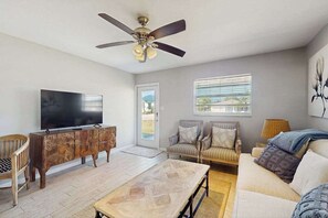 A living room with a television, wooden cabinet, sofa, and a ceiling fan. - Coastal duplex with full kitchen, close to beach & shopping (Naples)