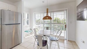 A modern kitchen with a stainless steel refrigerator, a round dining table with white chairs, and a large window with blinds. - Spacious Duplex with two kitchens, W/D, and WiFi throughout (Englewood)