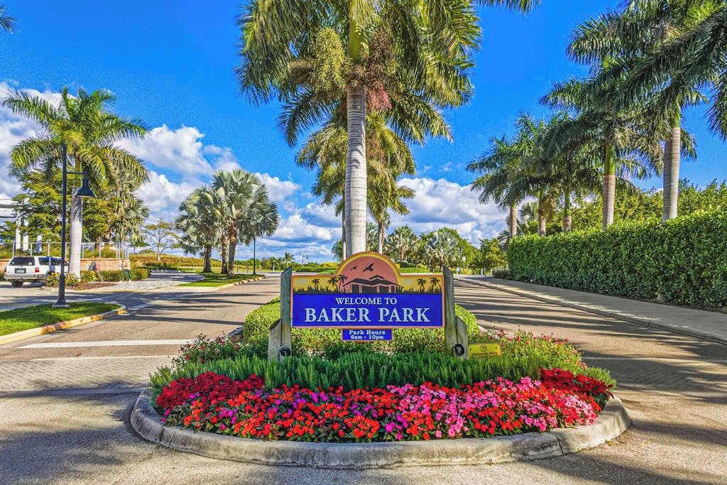 Señal de bienvenida a Baker Park, con un camino que atraviesa palmeras.