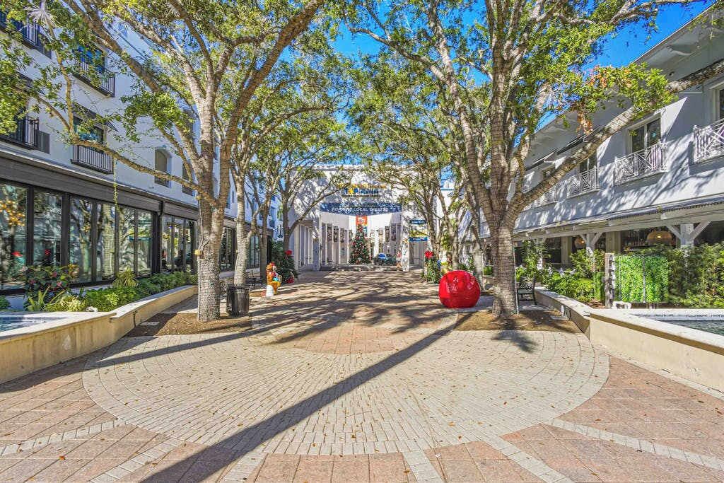 A tree-lined pedestrian walkway with buildings on either side, a fountain, and a red spherical sculpture.
