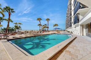 Ein Pool mit Liegestühlen und Palmen, umgeben von einem Gebäude mit Balkonen.