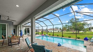 Et overdækket udendørsområde med swimmingpool, liggestole og et spisebord.