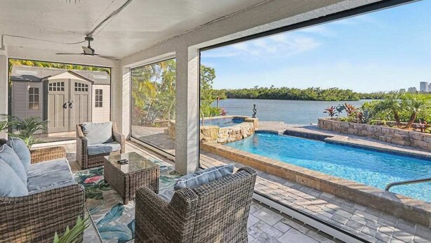 A covered outdoor area with wicker furniture, a swimming pool, and a view of a body of water. - Immaculate bay front home w/in ground pool, spa, paver patio & porch (Bonita Springs)
