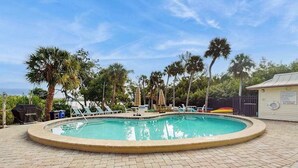 Ein kreisrunder Pool mit Liegestühlen und Sonnenschirmen, umgeben von Palmen und einer Ziegelterrasse.