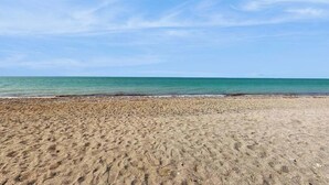 Ein sandiger Strand mit blauem Himmel und ruhigem Meer.
