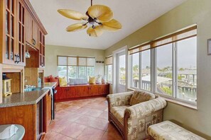 Ein geräumiges Zimmer mit einer Küche, einem großen Fenster mit Blick auf eine Brücke, einem Deckenventilator und einer Sitzecke mit Sofa und Sesseln.