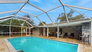 A swimming pool with a glass enclosure, stone walls, and outdoor furniture. - Relax, Swim & Explore! A Dog-Friendly Private Pool Retreat Close to Everything! (Port Charlotte)